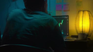 Avrupalı bir kripto tüccarı karanlık bir odada, elinde neon ışığı olan bir dizüstü bilgisayarın arkasında oturur, kripto döviz değişimindeki fiyat hareketlerinin grafiklerini gösteren bir ekrana bakar. Bir sigara içiyor. Bulanık arkaplan