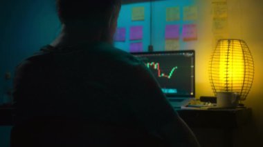 Avrupalı bir kripto tüccarı karanlık bir odada, elinde neon ışığı olan bir dizüstü bilgisayarın arkasında oturur, kripto döviz değişimindeki fiyat hareketlerinin grafiklerini gösteren bir ekrana bakar. Bir sigara içiyor. Bulanık arkaplan