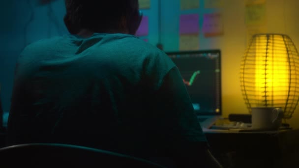 欧洲的加密商人坐在一个带有霓虹灯的黑暗房间里的笔记本电脑后面 看着一个屏幕 屏幕上有加密货币交易所的价格变动图 抽一支香烟 模糊的背景 — 图库视频影像
