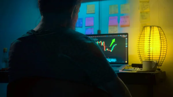 Avrupalı bir kripto tüccarı karanlık bir odada, elinde neon ışığı olan bir dizüstü bilgisayarın arkasında oturur, kripto döviz değişimindeki fiyat hareketlerinin grafiklerini gösteren bir ekrana bakar. Bir sigara içiyor. Bulanık arkaplan