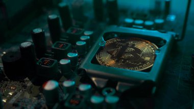 Karanlıkta mavi ışığı olan elektronik bileşenleri olan bir ana kartta merkezi işlemci yerine parlayan ve yansıtan altın bir Bitcoin. Bitcoin madenciliği.