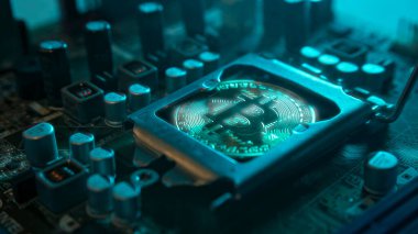 Karanlıkta mavi ışığı ve dumanı olan elektronik parçaları olan ana kartta merkezi bir işlemci yerine parlayan ve yansıtan altın bir Bitcoin. Bitcoin Madencilik