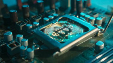 Karanlıkta mavi ışığı olan elektronik bileşenleri olan bir ana kartta merkezi işlemci yerine parlayan ve yansıtan altın bir Bitcoin. Bitcoin madenciliği.