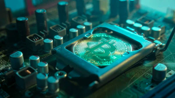 Karanlıkta mavi ışığı ve dumanı olan elektronik parçaları olan ana kartta merkezi bir işlemci yerine parlayan ve yansıtan altın bir Bitcoin. Bitcoin Madencilik