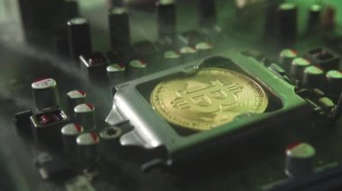 Karanlıkta ışık ve duman olan elektronik bileşenleri olan ana kartta merkezi bir işlemci yerine parlayan ve yansıtan altın bir Bitcoin. Bitcoin Madencilik