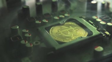 Karanlıkta ışık ve duman olan elektronik bileşenleri olan ana kartta merkezi bir işlemci yerine parlayan ve yansıtan altın bir Bitcoin. Bitcoin Madencilik