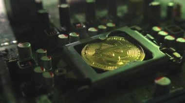 Karanlıkta ışık ve duman olan elektronik bileşenleri olan ana kartta merkezi bir işlemci yerine parlayan ve yansıtan altın bir Bitcoin. Bitcoin Madencilik
