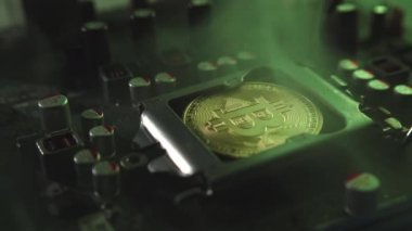 Karanlıkta ışık ve duman olan elektronik bileşenleri olan ana kartta merkezi bir işlemci yerine parlayan ve yansıtan altın bir Bitcoin. Bitcoin Madencilik