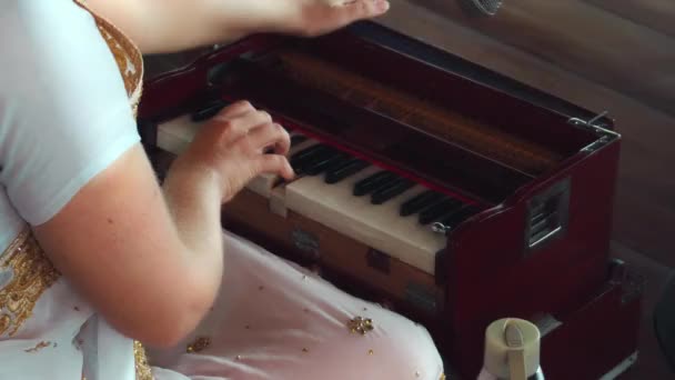 木製の床に座ってキーボードの民族楽器のハーモニウムを演奏する少女 — ストック動画