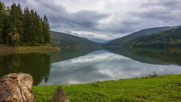 Mountain forest lake on a cloudy day. Clouds run quickly across the sky and are reflected in the water surface. Time lapse — Stock Footage Mountain Forest Lake Cloudy Day Clouds Run Quickly Sky Reflected Video Clip