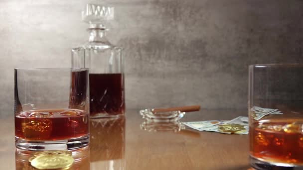 氷とお金でウィスキーを2杯 背景にはウイスキーとシガーの入った灰皿のボトル トランプのデッキがテーブルの上に落ちる スローモーション — ストック動画