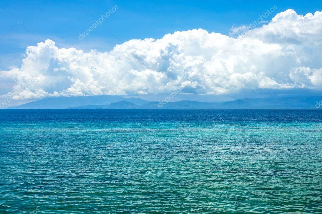 Sunny day in Indonesia. Turquoise water of calm ocean. Surprisingly beautiful clouds over the distant shore