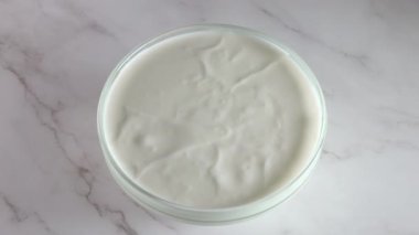 Mermer bir masada yoğurtlu cam kase. Muz dilimi düştü ve yüksek bir sıçrama yarattı. Yavaş çekim