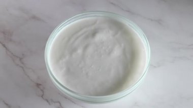 Mermer bir masada yoğurtlu cam kase. Birkaç badem fıstığı düşer ve bolca sprey püskürtür. Yavaş çekim