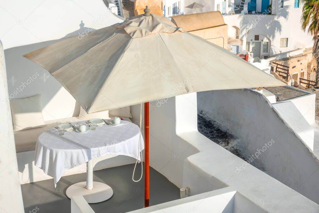 Greece. Sunny summer day on the caldera of Santorini island. Served table with a tablecloth under an umbrella on the open terrace
