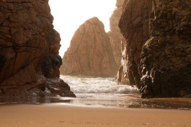 Sörf ve güneş tarafından arkadan aydınlatmalı kayalarda
