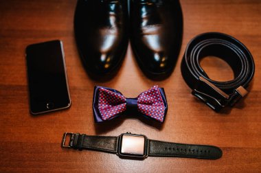 Şık erkek ayakkabıları, saat, damat için papyon. Düğün aksesuarları ve ahşap arka planda telefon. Üst görünüm.