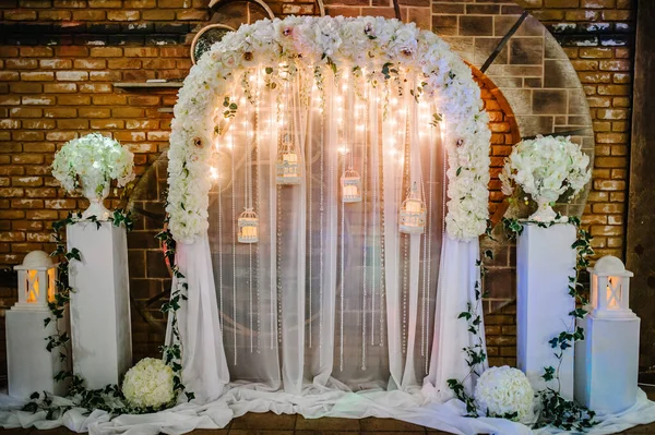 Arch for wedding area a is decorated with white flowers and greenery. Wedding ceremony with a vintage candles.