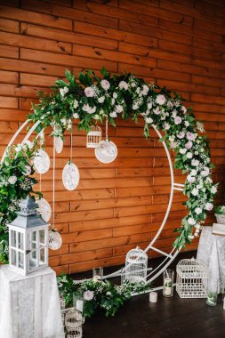 Düğün kemeri, süslenmiş beyaz çiçekler, yeşillikler, yeşillik. Fotoğraf duvarı, yer ya da yer, ahşap duvarın arka planında mumlar. Boho stilinde düğün süsü: Rüya Avcıları.