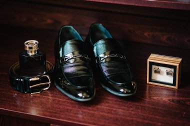 Beyaz ahşap arka planda izole edilmiş zarif siyah erkek aksesuarları. Kol düğmeleri, kemer, ayakkabı, parfüm. Düğün konsepti hazırlığı.