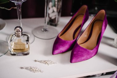 Düğün aksesuarı gelin. Şık menekşe ayakkabılar, küpeler ve parfümler ahşap arka plan masasında duruyor..