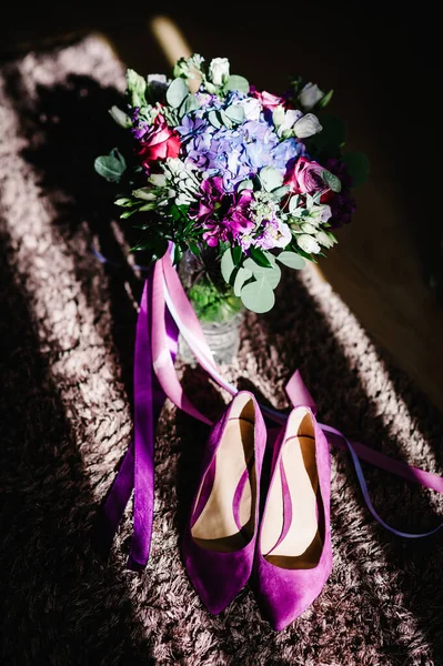 Female Purple velvet Wedding shoes on beige background and bouquet flowers. Bride accessories. Top view.