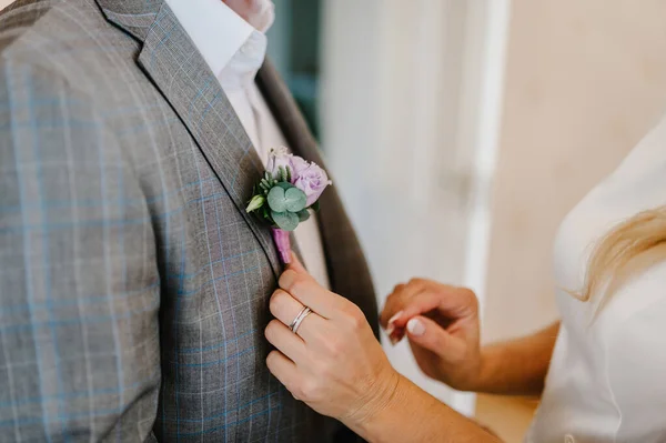 Bride\'s hands puts the groom on jacket a wedding boutonniere. Wedding concept.