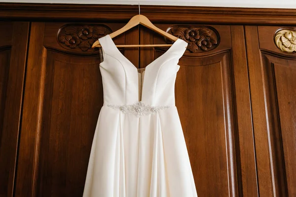 ホテルの木製の部屋でハンガーにかかってファッショナブルな美しい古典的なレースシルクの結婚式のドレス 朝の準備結婚式のコンセプト — ストック写真