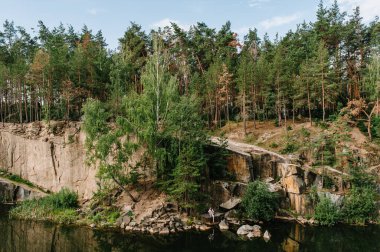Bir adam ve bir kadın kayalıklarda, ağacın altında, ormanın ve gölün yanında oturuyorlar. Eski bir endüstriyel granit ocağının manzarası. Kanyon. Sonbaharın doğası. Metin ve tasarım için yer.