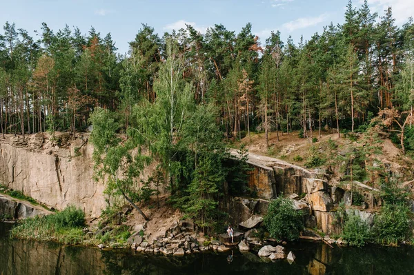 Bir adam ve bir kadın kayalıklarda, ağacın altında, ormanın ve gölün yanında oturuyorlar. Eski bir endüstriyel granit ocağının manzarası. Kanyon. Sonbaharın doğası. Metin ve tasarım için yer.