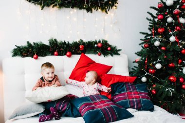 Çocuklar yatak odasında Noel ağacının yanında. Mutlu yıllar ve mutlu Noeller. Noel dekore edilmiş iç mekan. Aile tatili kavramı. Erkek ve kız kardeş.