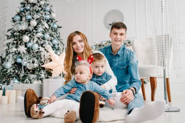 Baba, anne küçük oğlunu ve kızını Noel ağacının yanında tutuyor. Mutlu yıllar ve mutlu Noeller. Noel dekore edilmiş iç mekan. Aile tatili kavramı. Kapat..