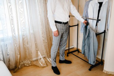 Eve bir ceket götüren adam. Tişörtlü damat odada duruyor. Kapatın. Takım elbiseli yakışıklı bir adam. Kıyafet konsepti Düğün sabahında damat.