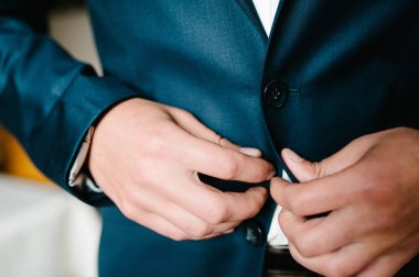 Adam düğme ceketini bağlıyor. Damat takım elbiseli, gömlek arka planda duruyor. Kapat..