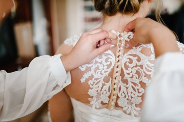 Nedime gelinin korsenin düğmelerini iliklemesine ve gelinliğini almasına yardım ediyor. Gelini düğün gününe hazırlıyor..