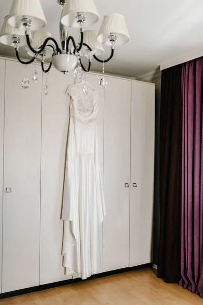 White silk wedding dress on hanger on a wooden background room. Beautiful gown bride before ceremony.