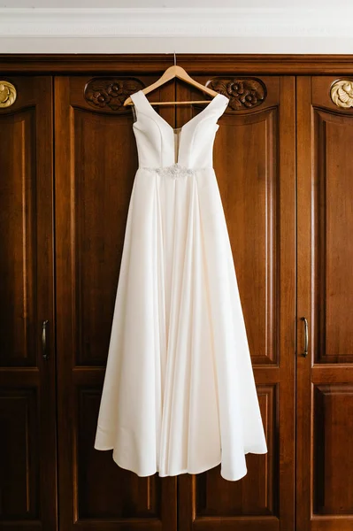 ホテルの木製の部屋でハンガーにかかってファッショナブルな美しい古典的なレースシルクの結婚式のドレス 朝の準備結婚式のコンセプト ヴィンテージウェディングドレス — ストック写真