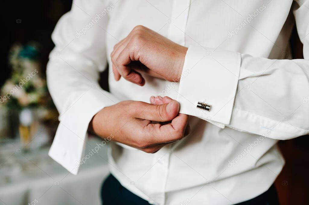 Handsome man buttoning cufflinks on white shirt. Groom's elegant male gold cufflink. wedding preparation morning of the groom.