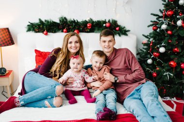 Baba ve anne, Noel ağacının yanındaki yatak odasında küçük oğlana ve kızına sarılıyor. Mutlu yıllar ve mutlu Noeller. Noel dekore edilmiş iç mekan. Aile tatili kavramı. Kapat..