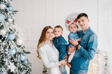 Baba ve anne Noel ağacının yanında küçük oğluna ve kızına sarılıyor. Mutlu yıllar ve mutlu Noeller. Noel dekore edilmiş iç mekan. Aile tatili kavramı. Kapat..