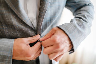 Adam düğmeleri bağlar. Damat takım elbiseli, gömlek beyaz arka planda duruyor. Kapat..