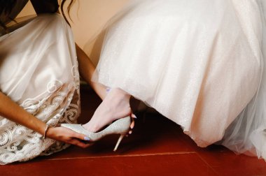 Nedimeler gelinin bacaklarını takar. Klasik gümüş ayakkabılar giyerler. Zarif kadın, arka plandaki beyaz elbiseye elini sürüyor. Düğün sabahı hazırlığı..