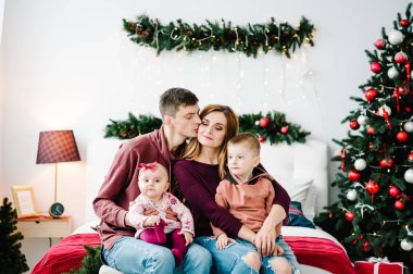 Baba, anne küçük oğlunu ve kızını Noel ağacının yanında tutuyor. Mutlu yıllar ve mutlu Noeller. Noel dekore edilmiş iç mekan. Aile tatili kavramı. Üst yarısı. Kapat..