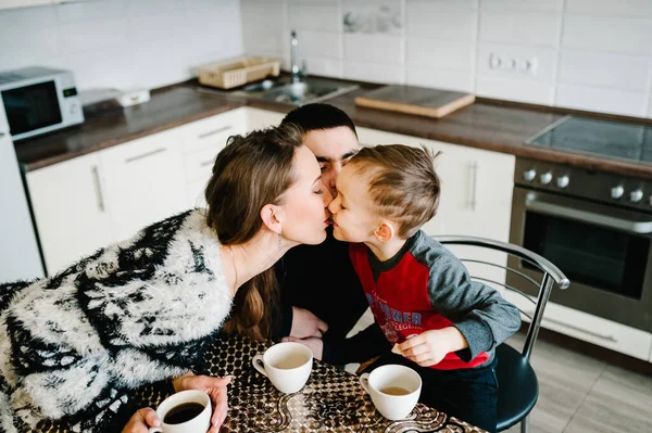 Young mom, dad and boy drinking coffee and tea in the morning. Happy mother, father and son having breakfast in the kitchen at home. Family, eating and people concept.