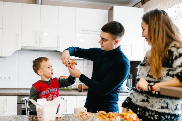 Young mom, dad and boy drinking coffee and tea in the morning. Happy mother, father and son having breakfast in the kitchen at home. Family, eating and people concept.