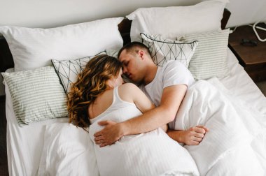 Sevgi dolu bir çift büyük bir yatak odasında yatakta sarılıp uyuyor. Sevgililer Günü Konsepti. yan görünüm.