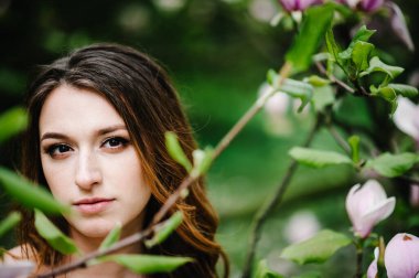 Çekici bir gelinin portresi manolya ve yeşilliklerin pembe çiçeklerinin arka planına karşı. Vesikalık. Doğa. Açık havada..