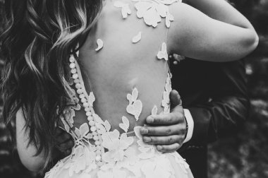 Arkasında arka görüş var. Düğün çifti parkta kucaklaşıyor arka planda, açık havada. Damat gelini kucaklıyor. Düğün töreni. Siyah beyaz fotoğraf.