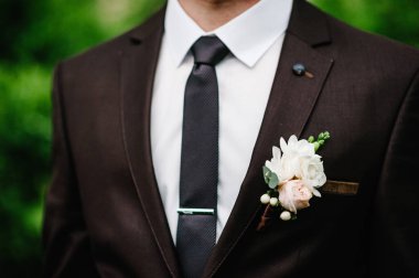 Damat ceketin yaka çiçeği ya da düğme deliği, bahçede arka planda duruyor..