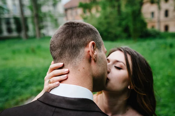 新郎を抱きかかえてキスをする魅力的な花嫁の肖像画は 庭の緑と背景のアーチに立っています 自然結婚式 — ストック写真